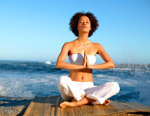 Meditating woman sitting cross-legged with back to the sea